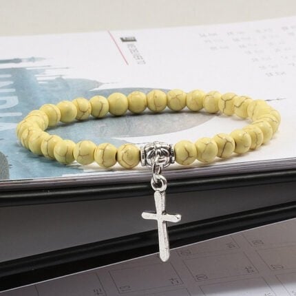 Bracelet religieux avec croix en perles jaunes sur un livre ouvert.