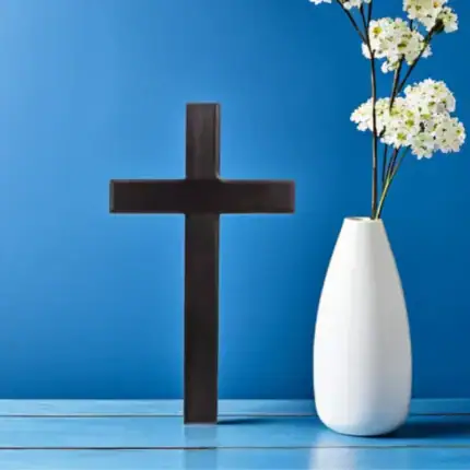 Croix chrétienne noire simple avec vase de fleurs blanches.