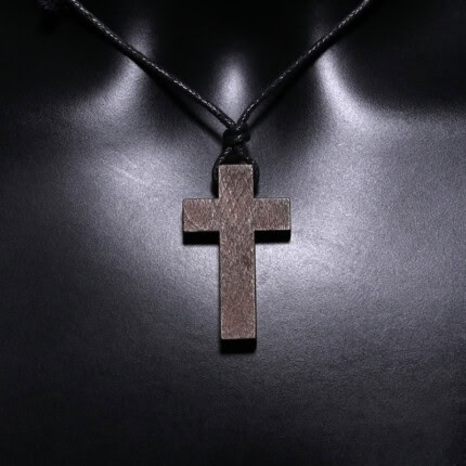 Croix en bois suspendue avec cordon noir sur fond sombre.